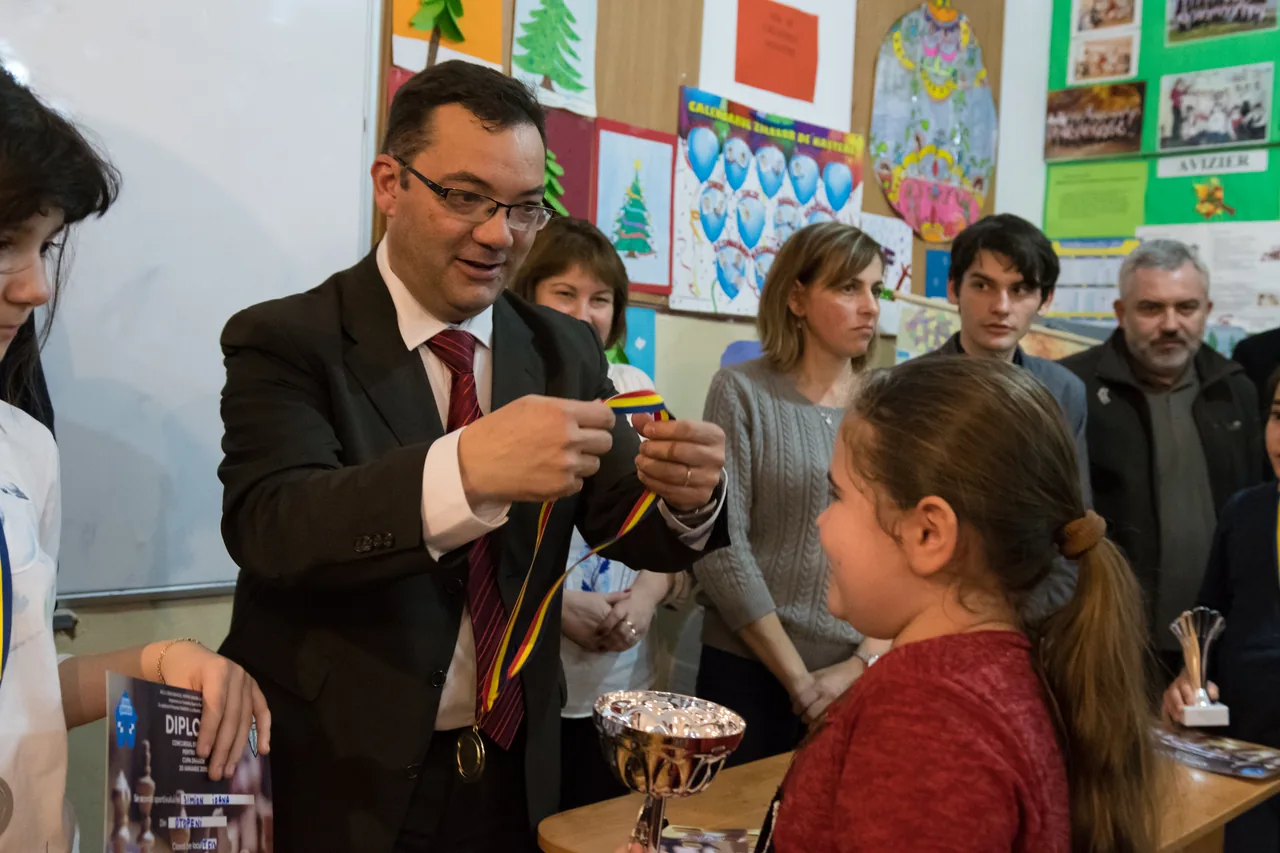 Moment de înmânare a unei medalii de șah, în prezența copiilor și adulților.